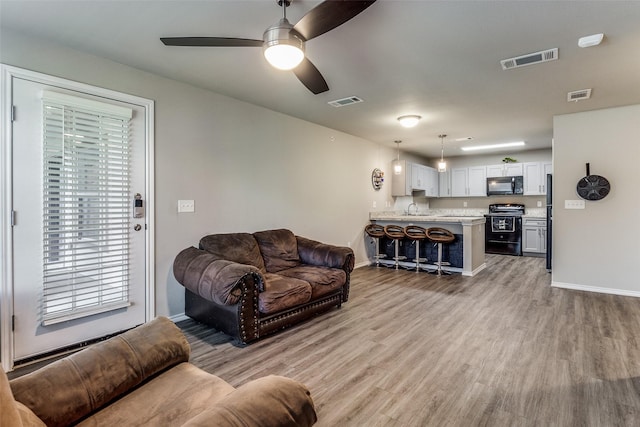 living room featuring ceiling fan, sink, and light hardwood / wood-style floors