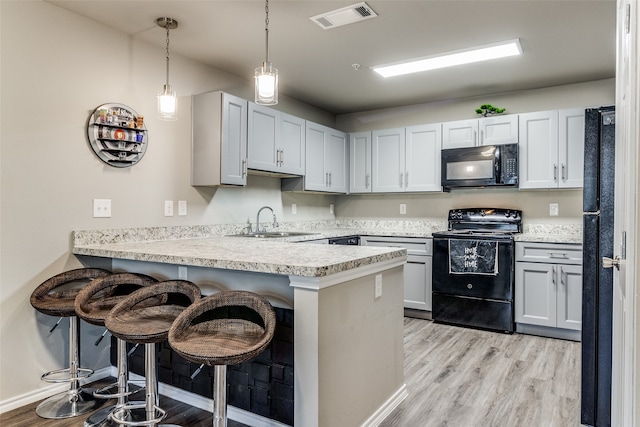 kitchen featuring sink, light hardwood / wood-style flooring, kitchen peninsula, a breakfast bar, and black appliances