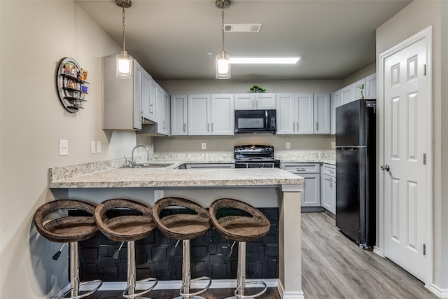 kitchen featuring sink, kitchen peninsula, a breakfast bar area, black appliances, and light wood-type flooring