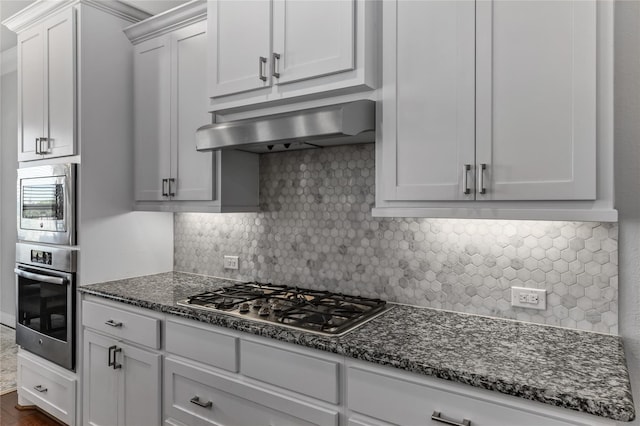 kitchen featuring dark stone counters, white cabinets, range hood, tasteful backsplash, and stainless steel appliances