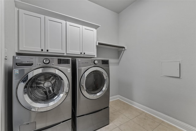 clothes washing area with washing machine and dryer, light tile patterned floors, and cabinets