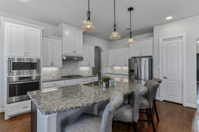 kitchen with appliances with stainless steel finishes, dark wood-type flooring, sink, white cabinets, and an island with sink