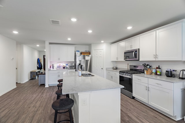 kitchen with white cabinetry, sink, stainless steel appliances, an island with sink, and hardwood / wood-style flooring