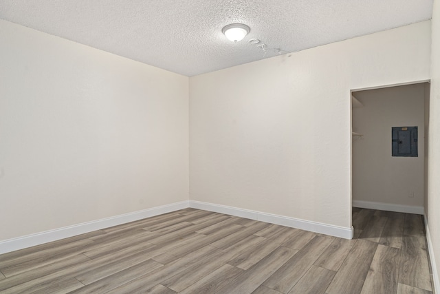 empty room featuring a textured ceiling, light hardwood / wood-style floors, and electric panel