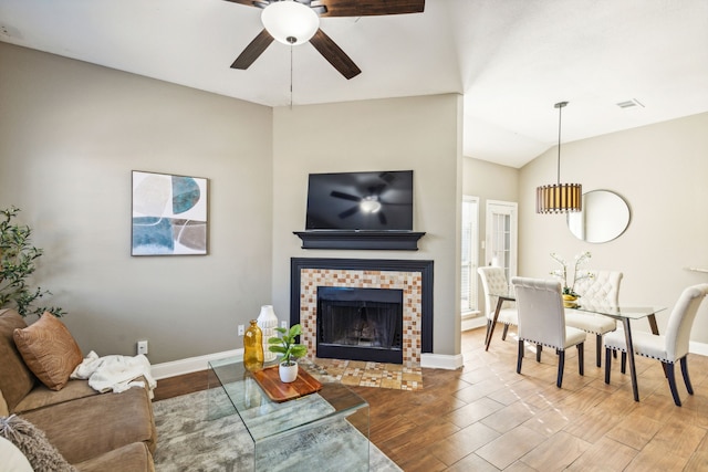 living room with vaulted ceiling, ceiling fan, and a tile fireplace