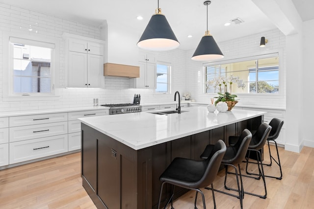 kitchen with a kitchen island with sink, sink, decorative light fixtures, white cabinets, and light hardwood / wood-style floors