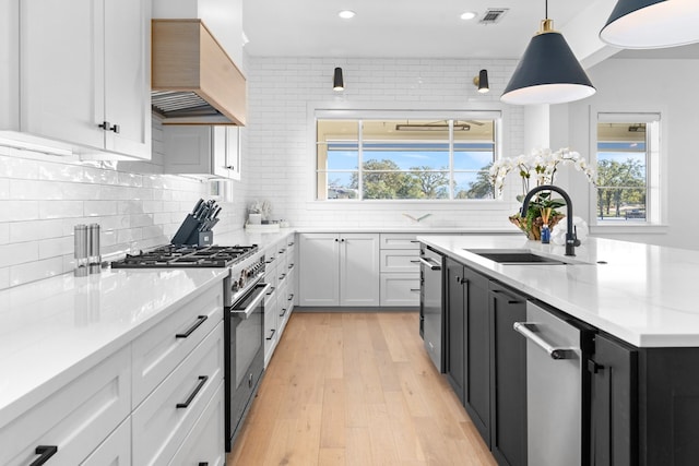 kitchen with custom range hood, high end stove, sink, white cabinets, and hanging light fixtures