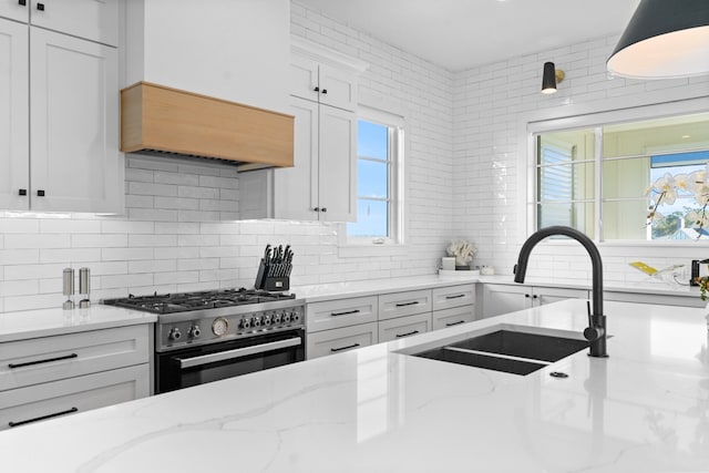 kitchen featuring stainless steel stove, decorative backsplash, a wealth of natural light, light stone counters, and white cabinetry