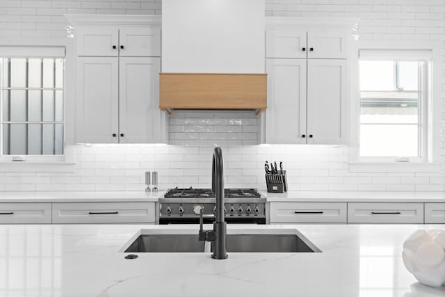 kitchen featuring tasteful backsplash, white cabinetry, light stone countertops, and stainless steel range oven