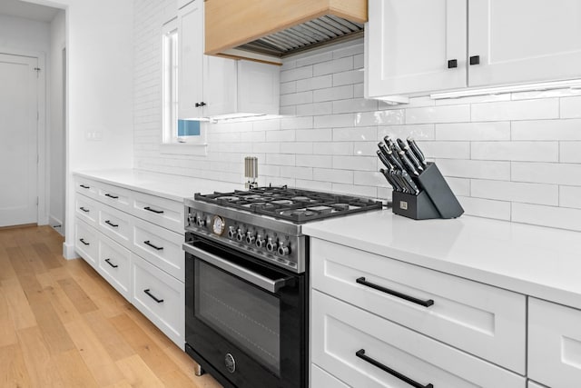 kitchen with tasteful backsplash, custom exhaust hood, high end stove, white cabinets, and light hardwood / wood-style floors