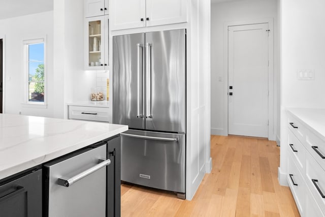 kitchen with white cabinets, stainless steel built in fridge, light stone countertops, light wood-type flooring, and tasteful backsplash