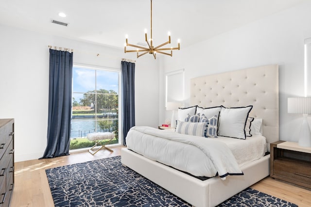 bedroom featuring a water view, a notable chandelier, and light wood-type flooring