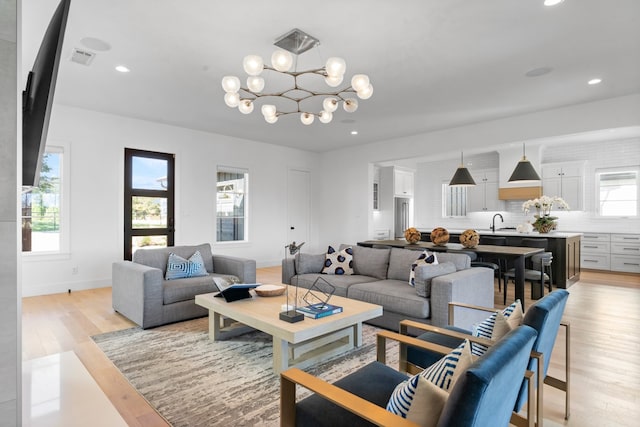 living room with sink, light hardwood / wood-style floors, and a notable chandelier