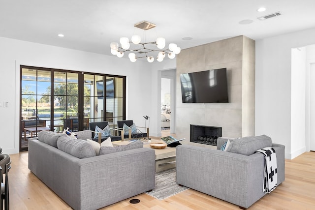 living room with light wood-type flooring, a tile fireplace, and an inviting chandelier