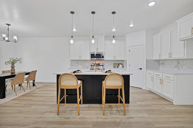 kitchen featuring decorative backsplash, appliances with stainless steel finishes, pendant lighting, light hardwood / wood-style floors, and white cabinetry