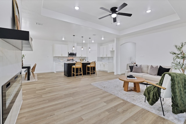 living room with light wood-type flooring, a tray ceiling, and ceiling fan