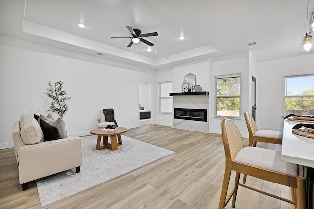 living room featuring a raised ceiling, ceiling fan, light hardwood / wood-style flooring, and a high end fireplace