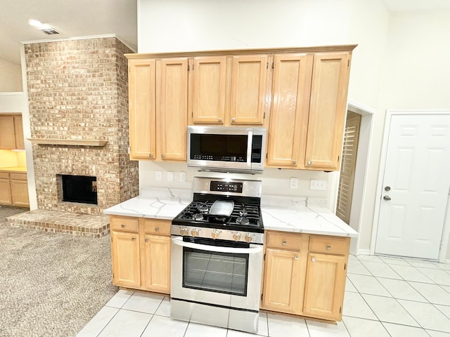 kitchen featuring light brown cabinets, light stone counters, a fireplace, light tile patterned floors, and appliances with stainless steel finishes