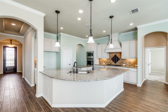 kitchen with sink, appliances with stainless steel finishes, light stone countertops, white cabinets, and a large island with sink