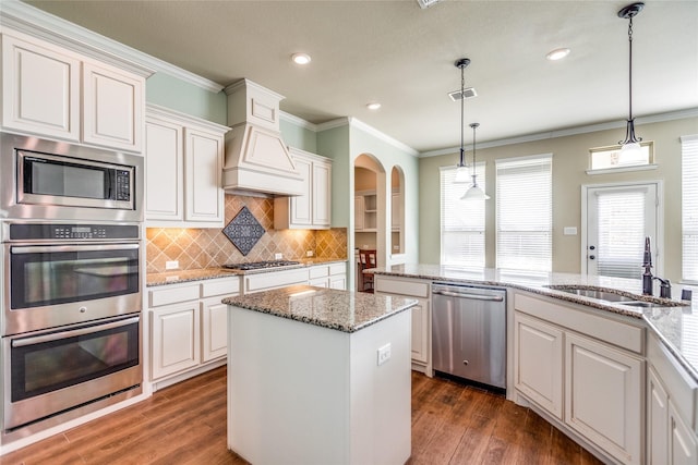 kitchen with decorative light fixtures, sink, custom exhaust hood, a center island, and stainless steel appliances