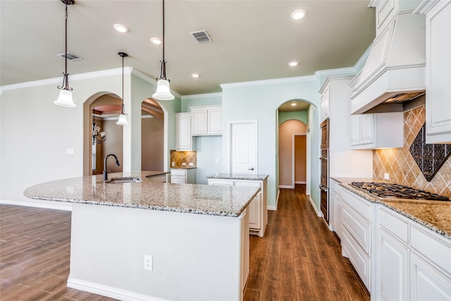 kitchen with premium range hood, pendant lighting, white cabinetry, sink, and a large island with sink