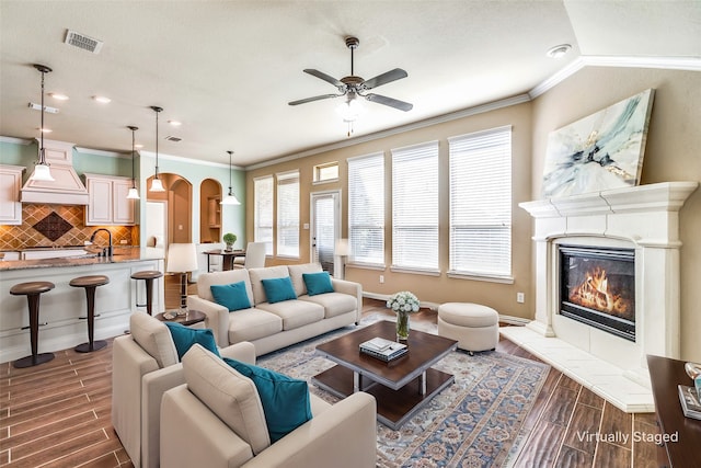 living room featuring ornamental molding, sink, ceiling fan, and a fireplace