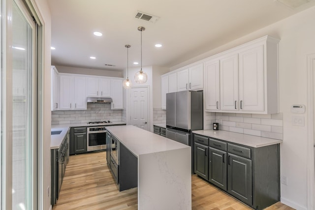 kitchen featuring appliances with stainless steel finishes, light hardwood / wood-style floors, white cabinets, a kitchen island, and decorative light fixtures