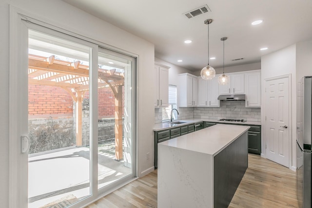 kitchen with sink, gas cooktop, hanging light fixtures, white cabinets, and a kitchen island