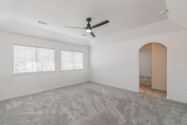 unfurnished room featuring a tray ceiling, vaulted ceiling, light colored carpet, and ceiling fan