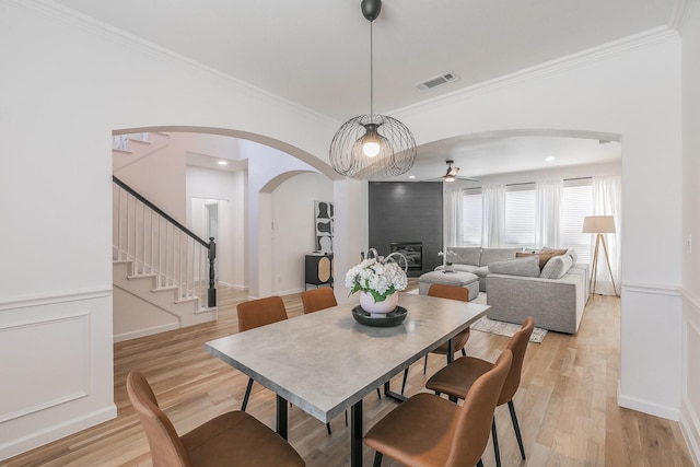 dining room with ornamental molding, ceiling fan, a fireplace, and light wood-type flooring