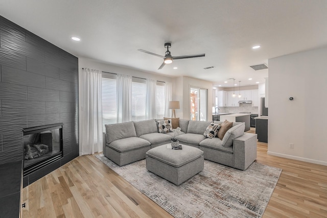 living room featuring ceiling fan, sink, a fireplace, and light hardwood / wood-style flooring