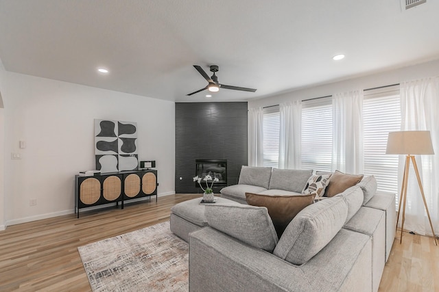 living room featuring ceiling fan, a large fireplace, and light wood-type flooring