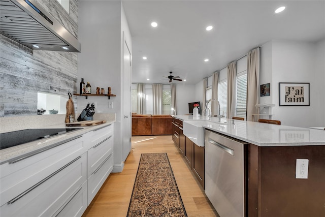 kitchen with stainless steel dishwasher, wall chimney exhaust hood, a center island with sink, light hardwood / wood-style flooring, and white cabinets