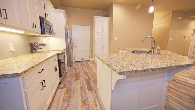 kitchen with pendant lighting, hardwood / wood-style floors, an island with sink, appliances with stainless steel finishes, and white cabinetry