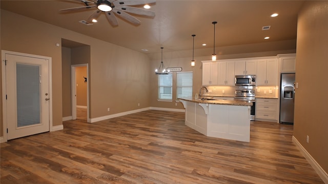 kitchen featuring stainless steel appliances, dark hardwood / wood-style flooring, a breakfast bar area, a kitchen island with sink, and white cabinets