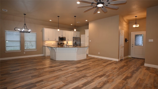 kitchen with a kitchen bar, appliances with stainless steel finishes, a center island with sink, dark stone countertops, and white cabinetry