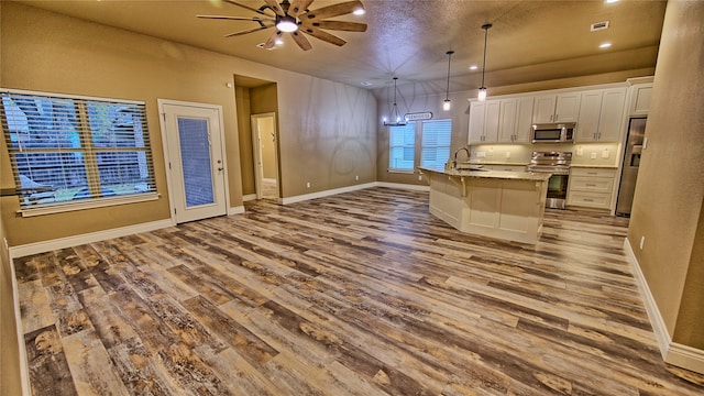 kitchen with stainless steel appliances, pendant lighting, wood-type flooring, a center island with sink, and white cabinets