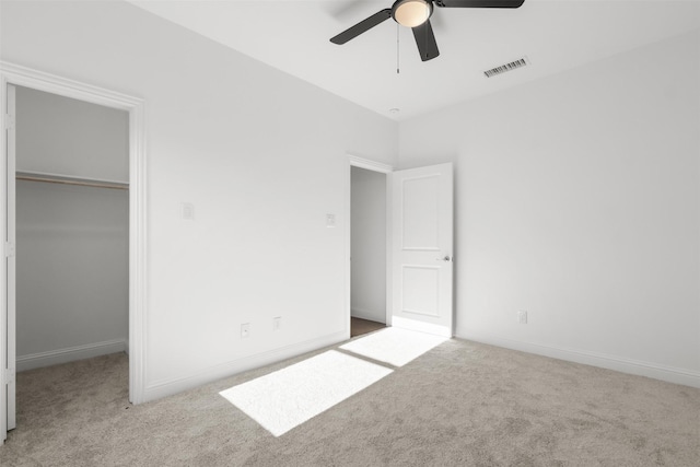 unfurnished bedroom with a walk in closet, ceiling fan, a closet, and light carpet