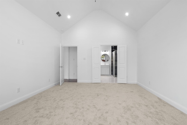 unfurnished bedroom with ensuite bathroom, light carpet, and high vaulted ceiling