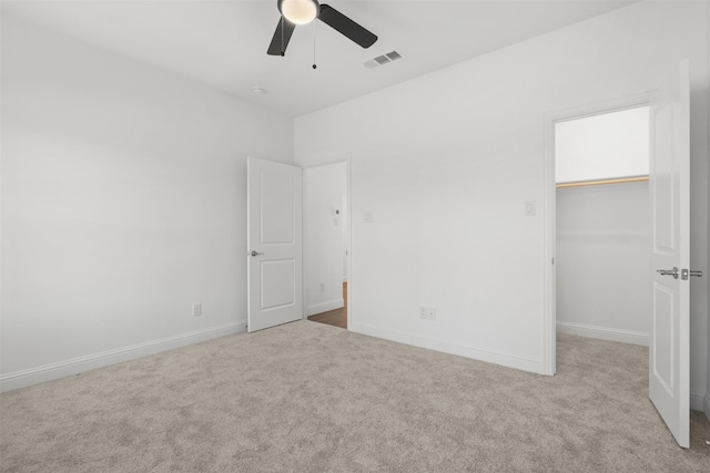 unfurnished bedroom with a spacious closet, a closet, ceiling fan, and light carpet