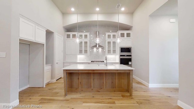 kitchen with white cabinets, light hardwood / wood-style floors, a center island with sink, and stainless steel appliances