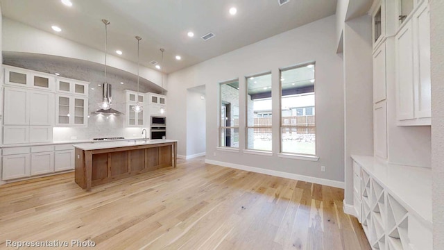 kitchen with pendant lighting, a center island, white cabinets, wall chimney exhaust hood, and light wood-type flooring