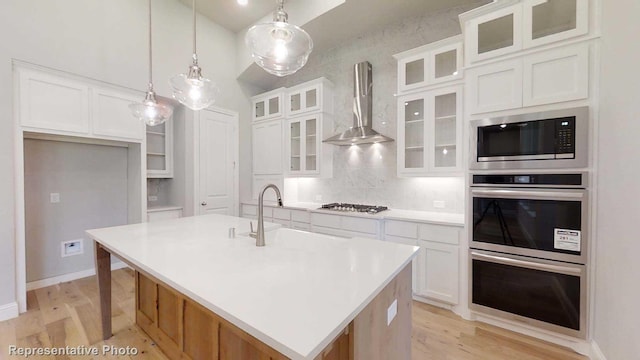 kitchen with decorative light fixtures, white cabinetry, a kitchen island with sink, and wall chimney range hood