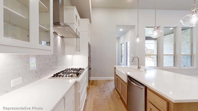 kitchen with appliances with stainless steel finishes, sink, wall chimney range hood, a center island with sink, and hanging light fixtures