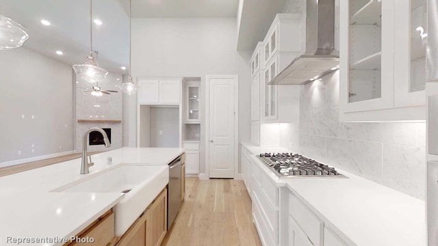 kitchen featuring appliances with stainless steel finishes, ceiling fan, wall chimney range hood, white cabinetry, and hanging light fixtures