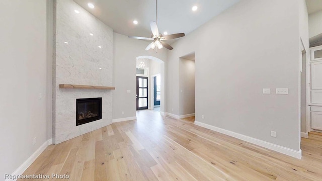 unfurnished living room featuring a tiled fireplace, ceiling fan, a high ceiling, and light wood-type flooring