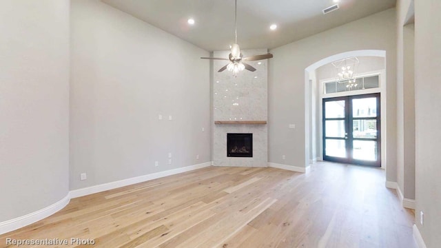 unfurnished living room with ceiling fan, light hardwood / wood-style floors, a tiled fireplace, and french doors