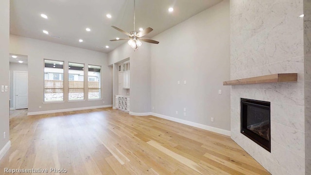 unfurnished living room featuring a tiled fireplace, ceiling fan, light hardwood / wood-style flooring, and high vaulted ceiling