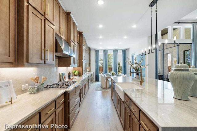 kitchen featuring sink, hanging light fixtures, stainless steel gas cooktop, light stone counters, and light wood-type flooring