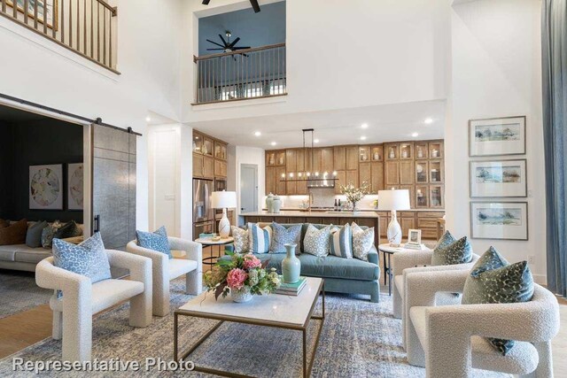 living room with ceiling fan, a barn door, and a high ceiling